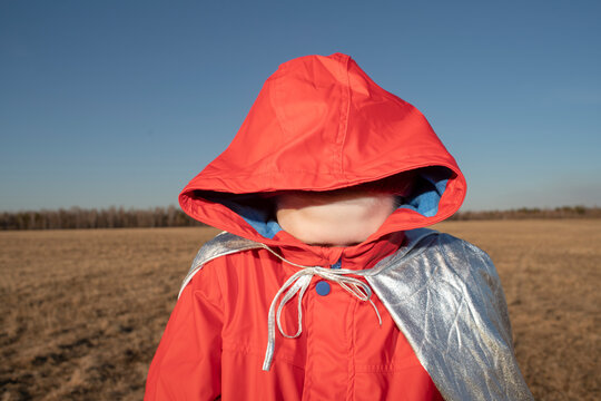 Boy dressed up as superhero in steppe landscape hiding his face in hood of his jacket