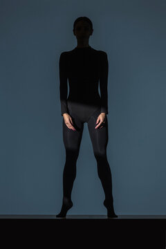Woman dressed in black standing on tiptoes in the shadow