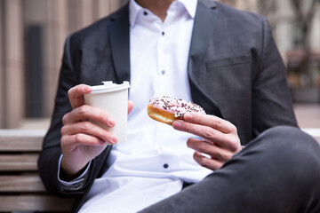 Businessman's hands holding doughnut and coffee to go, close-up