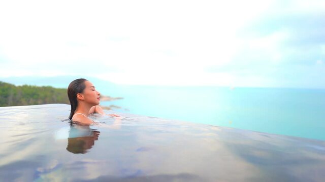 A woman fresh from swimming approaches the water edge of the pool giving her the panoramic view of the ocean and island edge. Title space