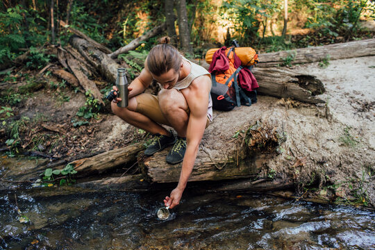 Young hiker scooping fresh water in a forest
