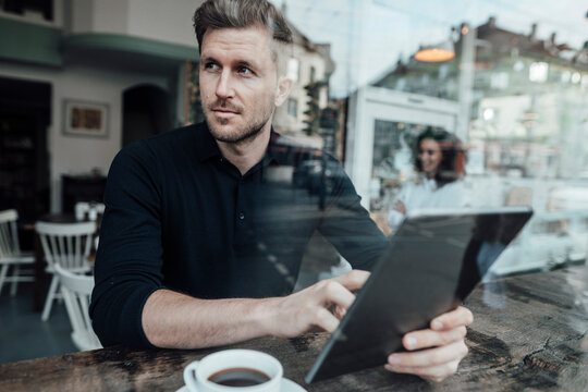 Businessman using digital tablet looking away while sitting at cafe