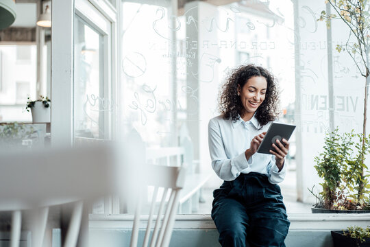 Smiling young businesswoman using digital tablet while sitting at cafe