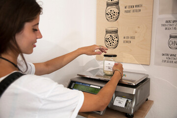 Young woman in packaging-free supermarket weighing goods on scale