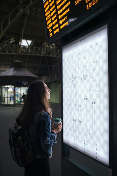 Young female traveller with coffee to got looking on destination board on the train station