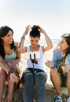Happy female friends with beer bottles taking a selfie on the beach