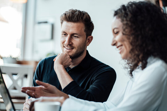 Smiling business people working on laptop while sitting at cafe