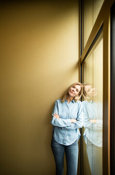 Businesswoman standing on a window, looking on camera, ams crossed