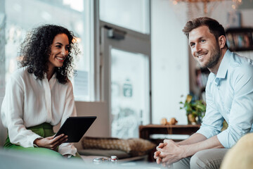 Businesswoman with digital tablet looking at colleague while sitting at cafe