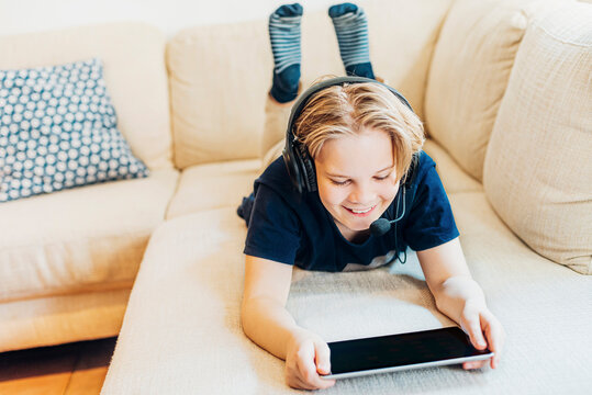 Boy lying on couch at home with headset and tablet