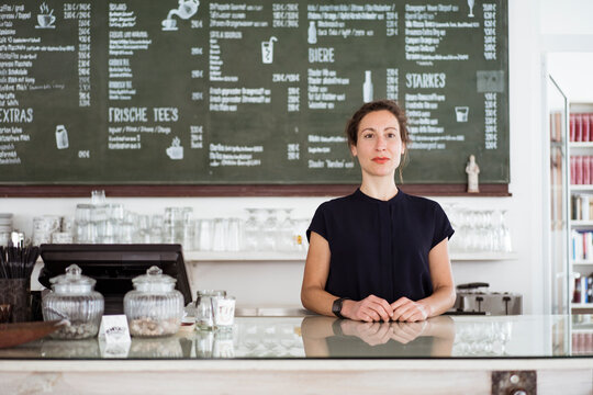Confident female owner standing at bar counter in coffee shop