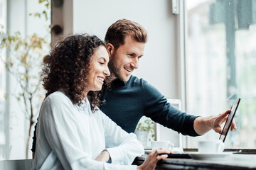 Smiling business people working on laptop while sitting at cafe