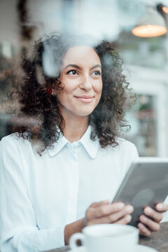 Businesswoman with digital tablet smiling while sitting at cafe