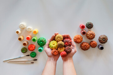 A young man holding in the palms DIY gypsum pumpkins painted in different bright colors of autumn palette over white background, Halloween and Thanksgiving Day ornament, craft decoration, copy space
