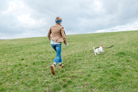 Back view of mature woman playing with her dog on a meadow