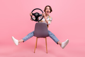 Full length body size photo woman riding on chair keeping steering wheel isolated pastel pink color background