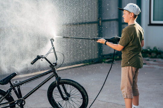 Boy washing bmx bike with pressure washer on yard