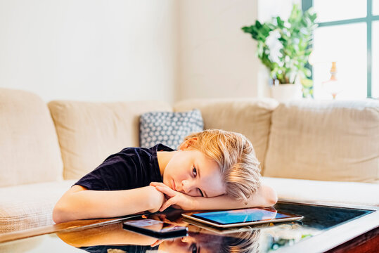 Serious boy lying on coffee table with smartphone and tablet