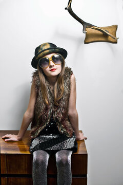 Portrait of girl wearing party clothing and oversized sunglasses sitting on sideboard