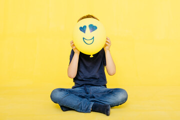 Boy holding yellow balloon with anthropomorphic face against colored background