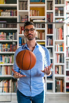 Portrait Of Young Man With Basketball Standing In Front Of Bookshelves At Home