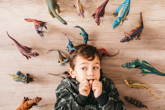 Portrait of anxious little boy lying on the floor between toy dinosaurs