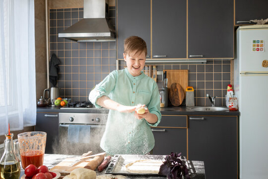 Portrait of laughing boy preparing pizza dough in kitchen