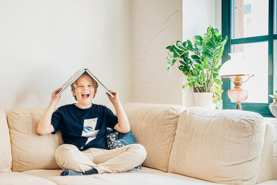 Portrait of laughing boy sitting on couch in living room with a book