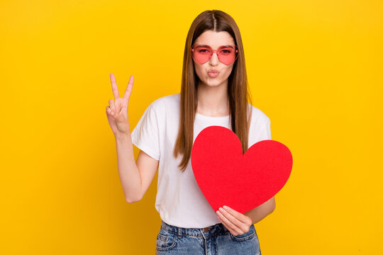 Photo of flirty young happy woman air kiss wear red paper heart v-sign isolated on yellow color background