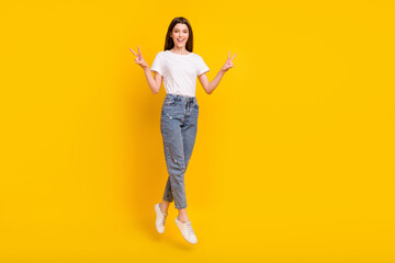 Full body photo of cheerful young happy woman jump up make v-signs good mood isolated on yellow color background