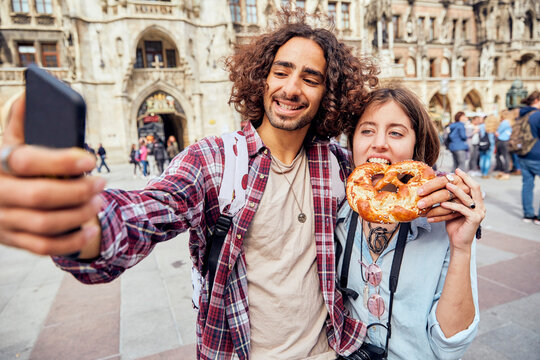 Young couple taking a selfie with brezel in the mouth, Munich, Germany