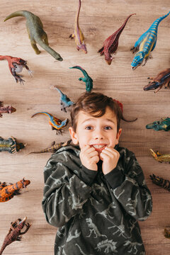 Portrait of anxious little boy lying on the floor between toy dinosaurs