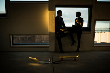 Colleagues sitting on window sill, discussing after work