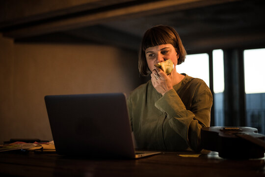 Businesswoman working late, eating apple