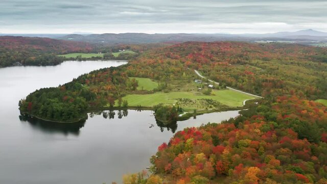 Aerial 4K View Above Scenic Countryside village at Lake surrounded by the Fall Forest. Top View Village houses in Colorful Countryside Autumn Forest. Fall Orange, Green, Yellow, Red Leaves Trees Woods