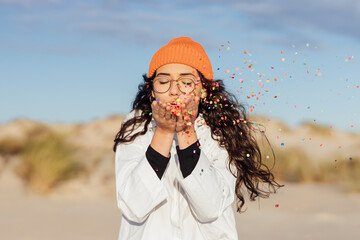 Young woman with eyes closed blowing confetti against sky