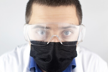 Close-up of a doctor wearing foggy goggles. The therapist in mask and eye protection looks directly...