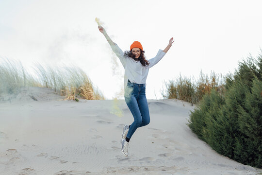 Happy young woman with smoke bomb jumping against sky