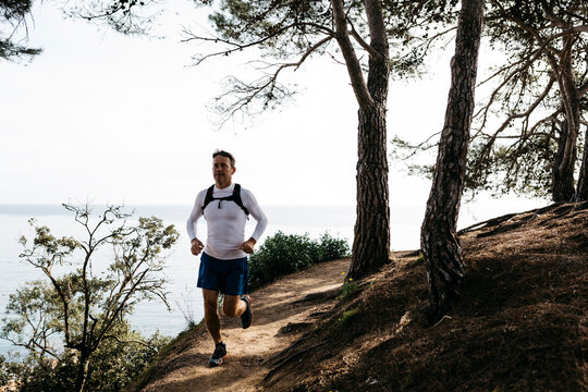 Man running on footpath near forest against clear sky