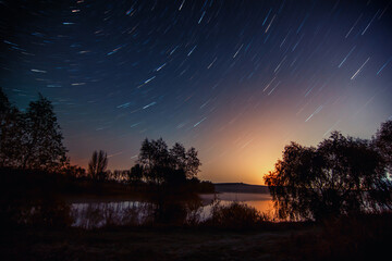 star trails over the night lake. Beautiful night landscape with star trail above lake.  Scenic...