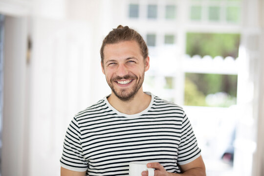 Portrait of smiling young man holding cup of coffee at home
