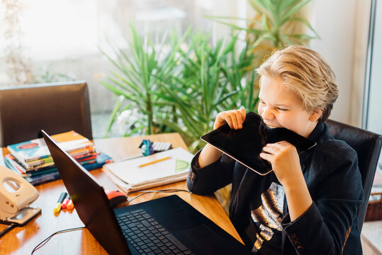 Angry boy sitting at desk biting in tablet