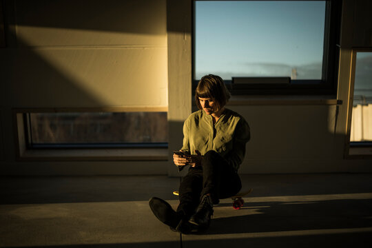 Businesswoman sitting on office floor at sunset, using smartphone