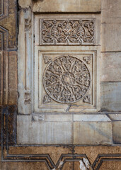 Round floral patterns framed by geometrical patterns carved into the exterior ancient stone wall of Sultan Hasan Mosque, Old Cairo, Egypt