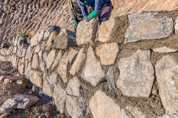 Workers are bulding a stone wall. Stone walls are a kind of masonry construction that has been used...