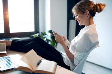 Smiling woman using phone at home office