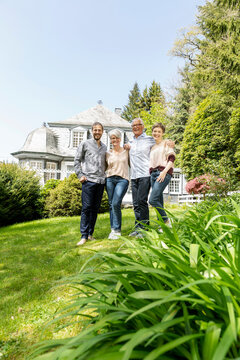 Happy senior couple with adult children standing in garden of their home