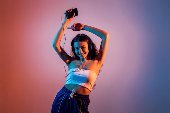 Teenage Girl Holding Smart Phone Dancing While Enjoying Music Against Colored Background