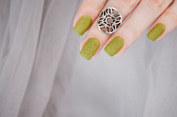Closeup top view of beautiful painted in green nails isolated on grey lace background. Winter autumn nail style.