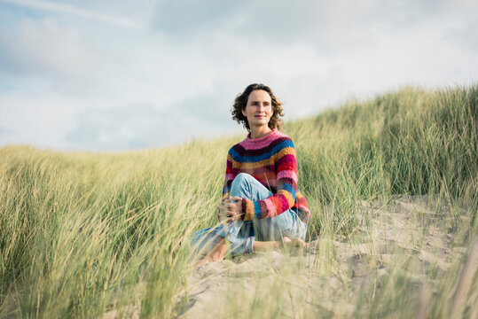 Mature woman relaxing on the beach, sitting in the dunes